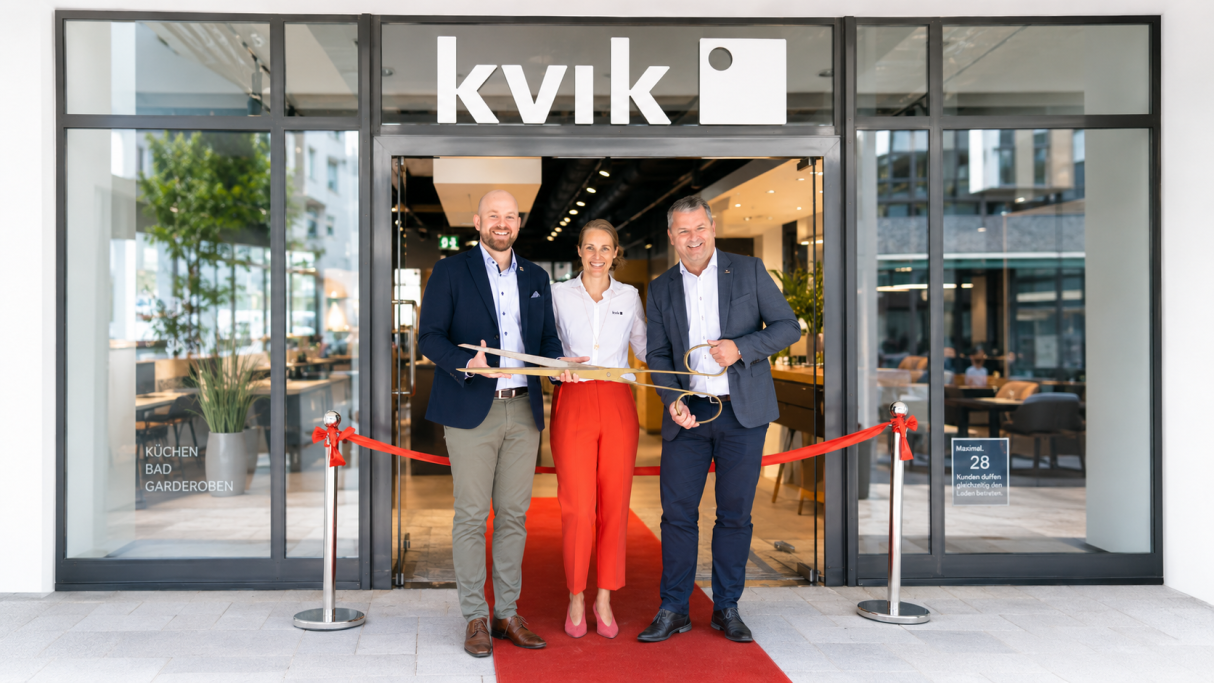 Drei Personen stehen vor dem Kvik-Geschäft, lächeln und halten Auszeichnungen.