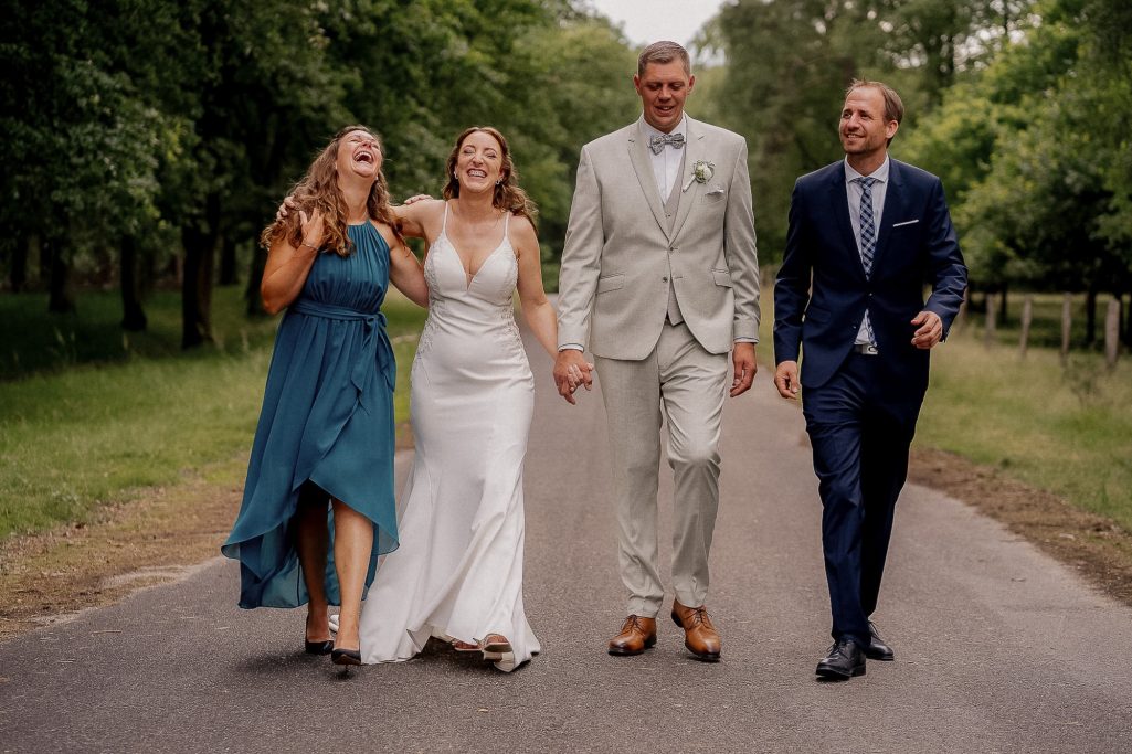 Vier Personen in eleganter Kleidung gehen lächelnd auf einem Weg durch einen Park.