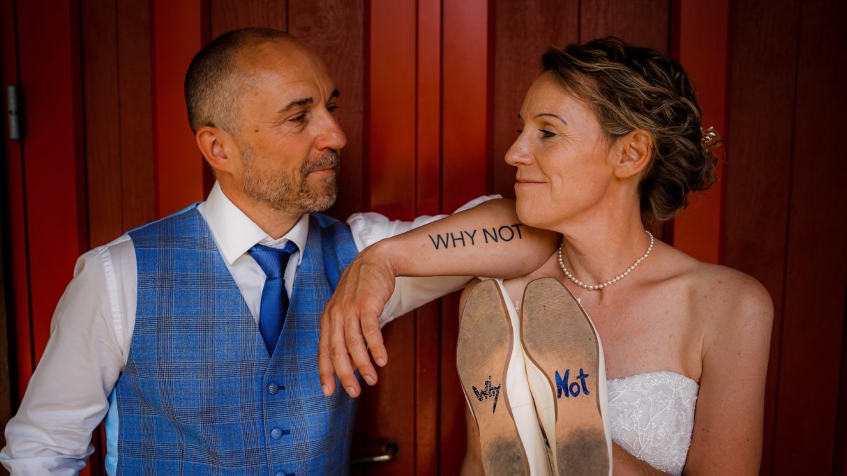 Braut und Bräutigam in eleganter Kleidung posieren an einer Holzwand.