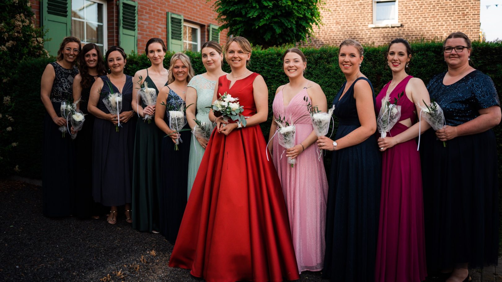 Gruppe von zehn Frauen in festlichen Kleidern, die Blumensträuße halten.
