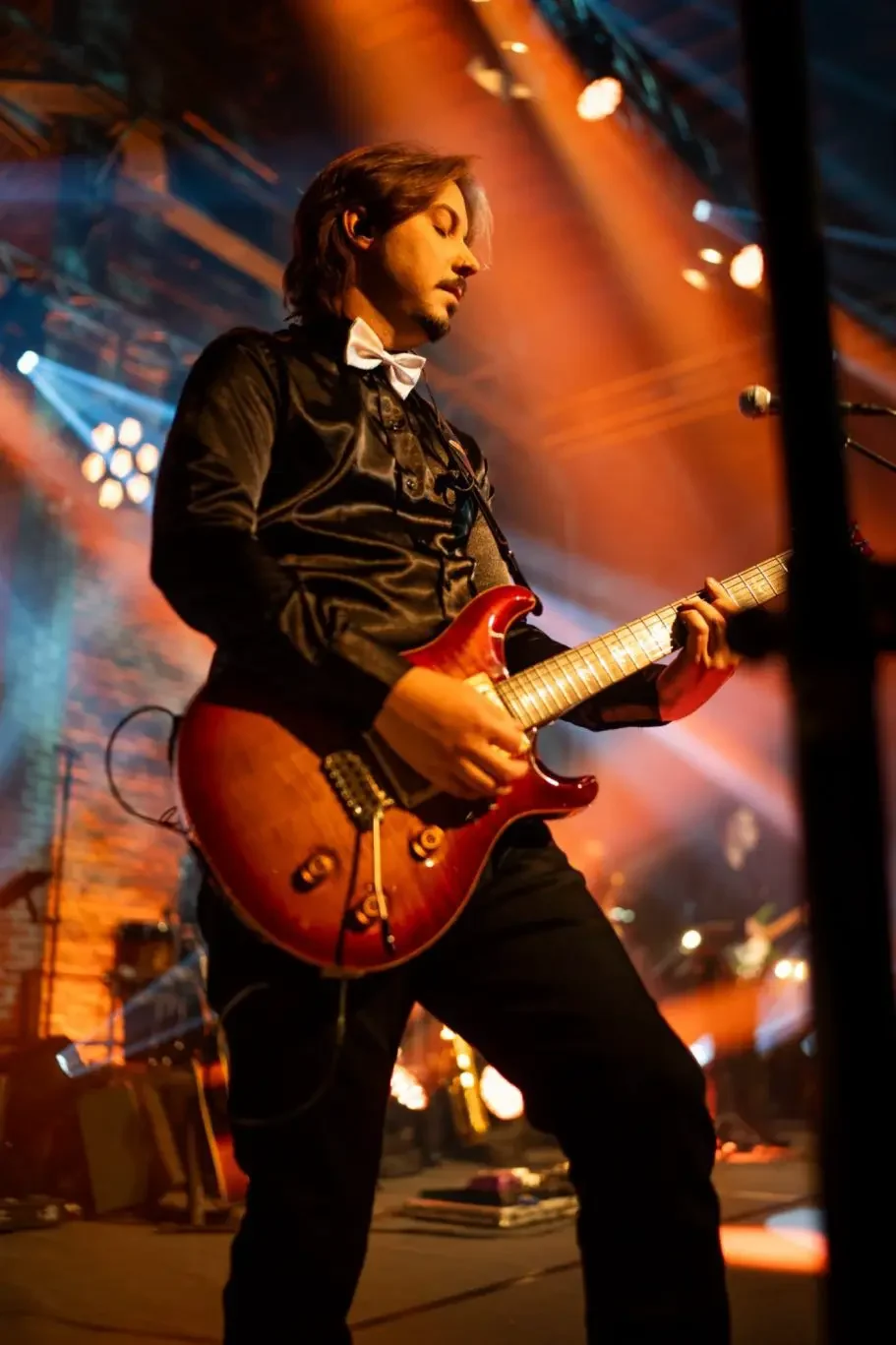 Musiker spielt E-Gitarre auf einer Bühne mit bunten Lichtern im Hintergrund.