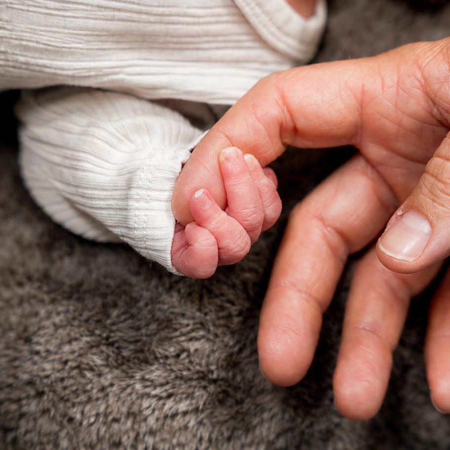 Ein neugeborenes Baby greift sanft einen Finger einer erwachsenen Hand.