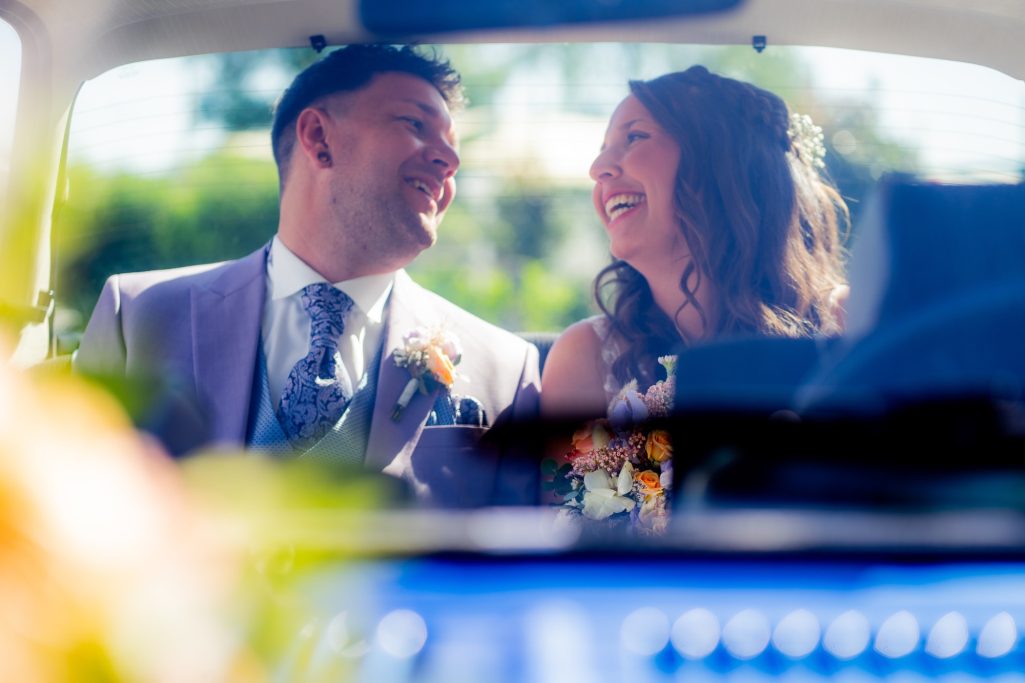 Brautpaar lächelt verliebt beim Fahren in einem Auto, fröhliche Stimmung.