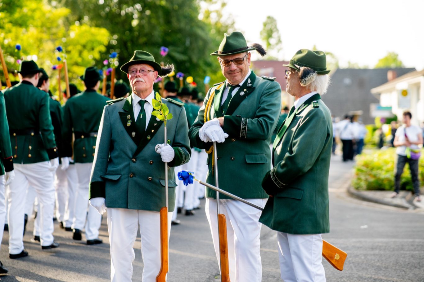 Drei Männer in grünen Anzügen mit Schützenflinten stehen bei einer Parade zusammen.