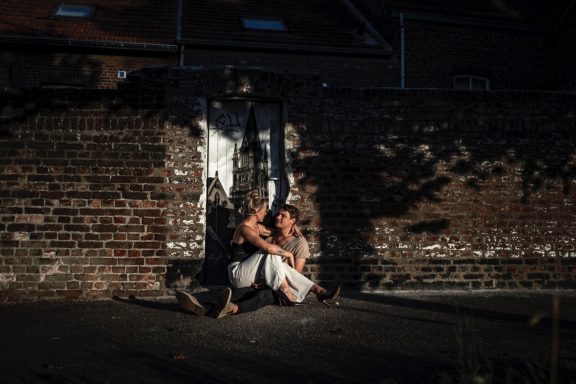 Eine Person sitzt an einer Mauer und hält eine andere Person in einem ruhigen Moment.