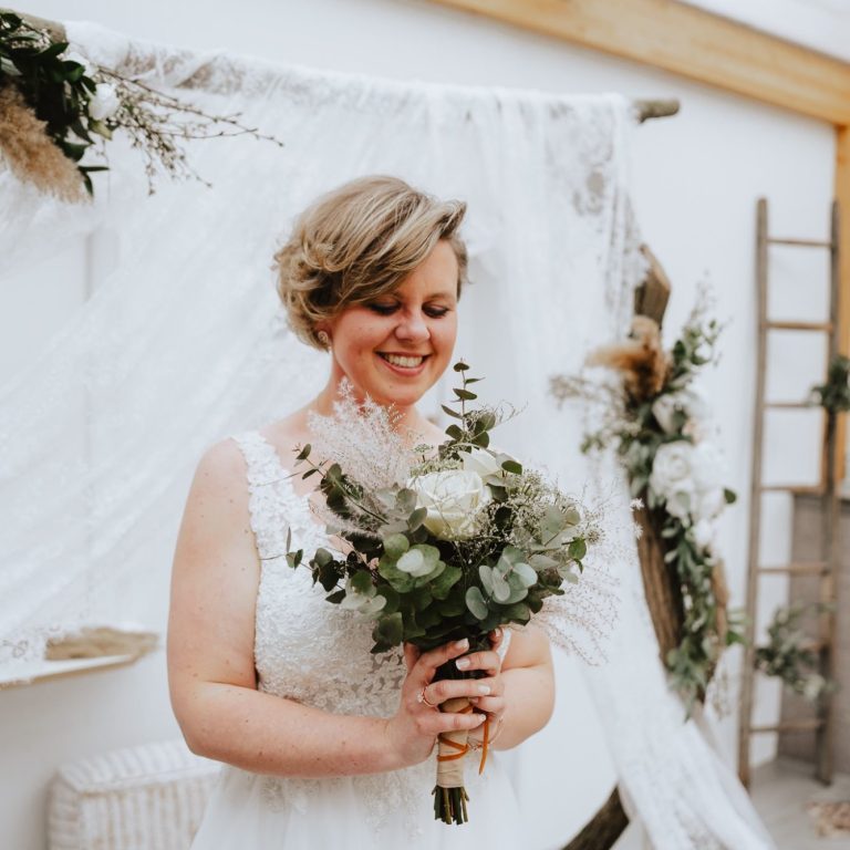 Lächelnde Braut mit Blumenstrauß in einem eleganten, dekorierten Raum.