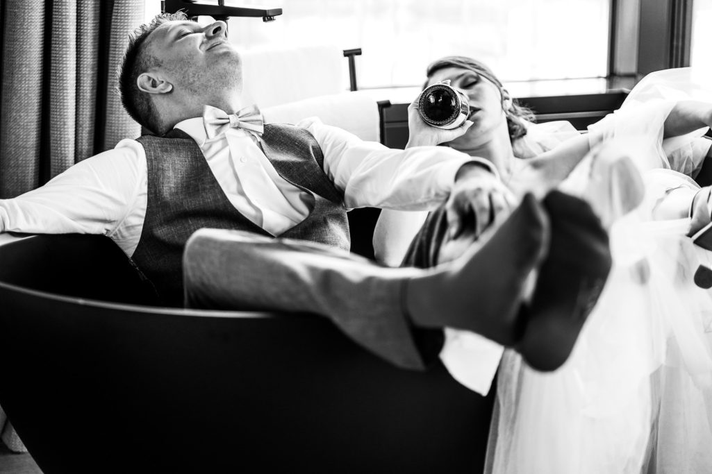 Ein Mann in einem Anzug sitzt entspannt in einer Badewanne, während eine Frau neben ihm liegt.