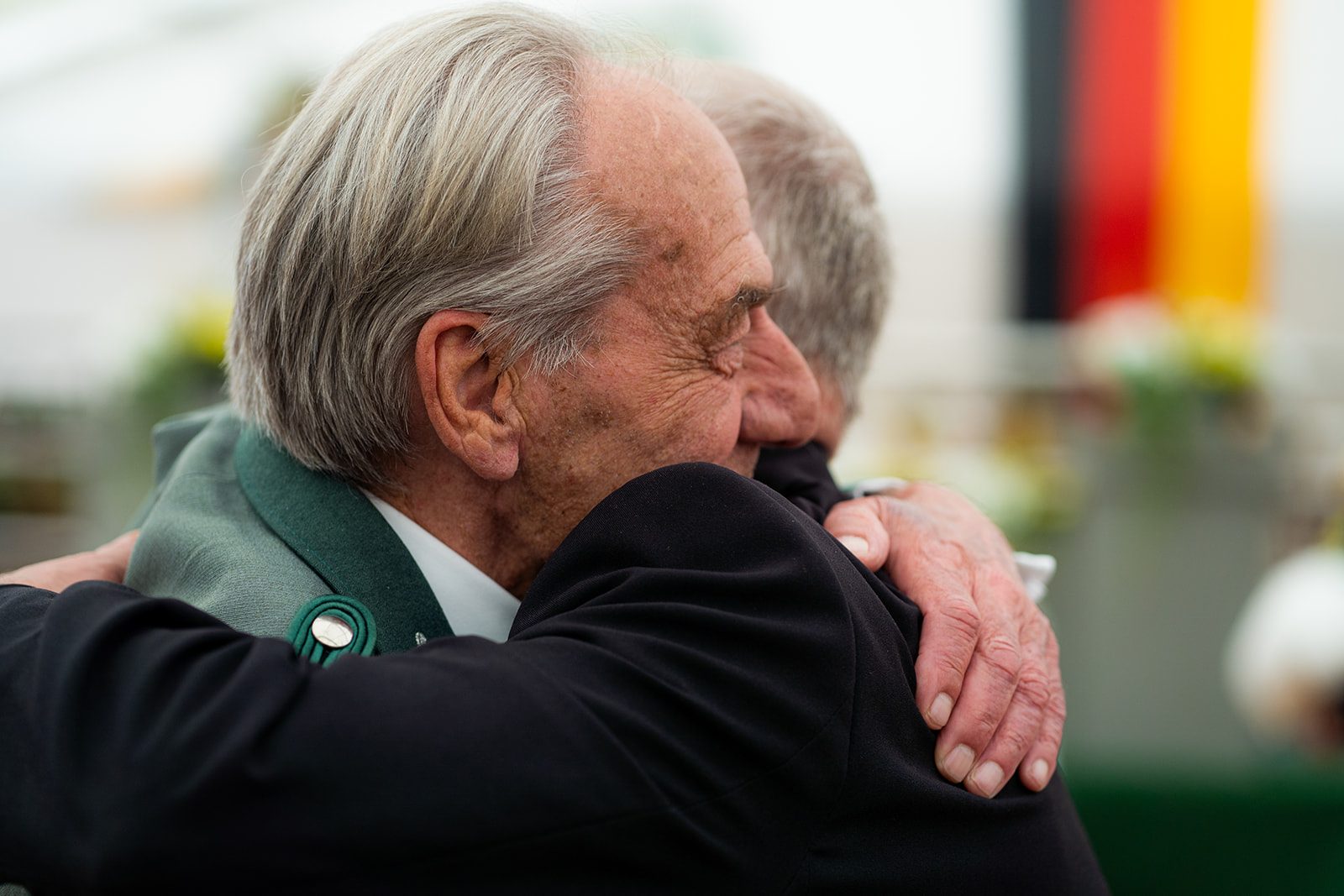 Zwei Männer umarmen sich herzlich, im Hintergrund Farben der deutschen Flagge.