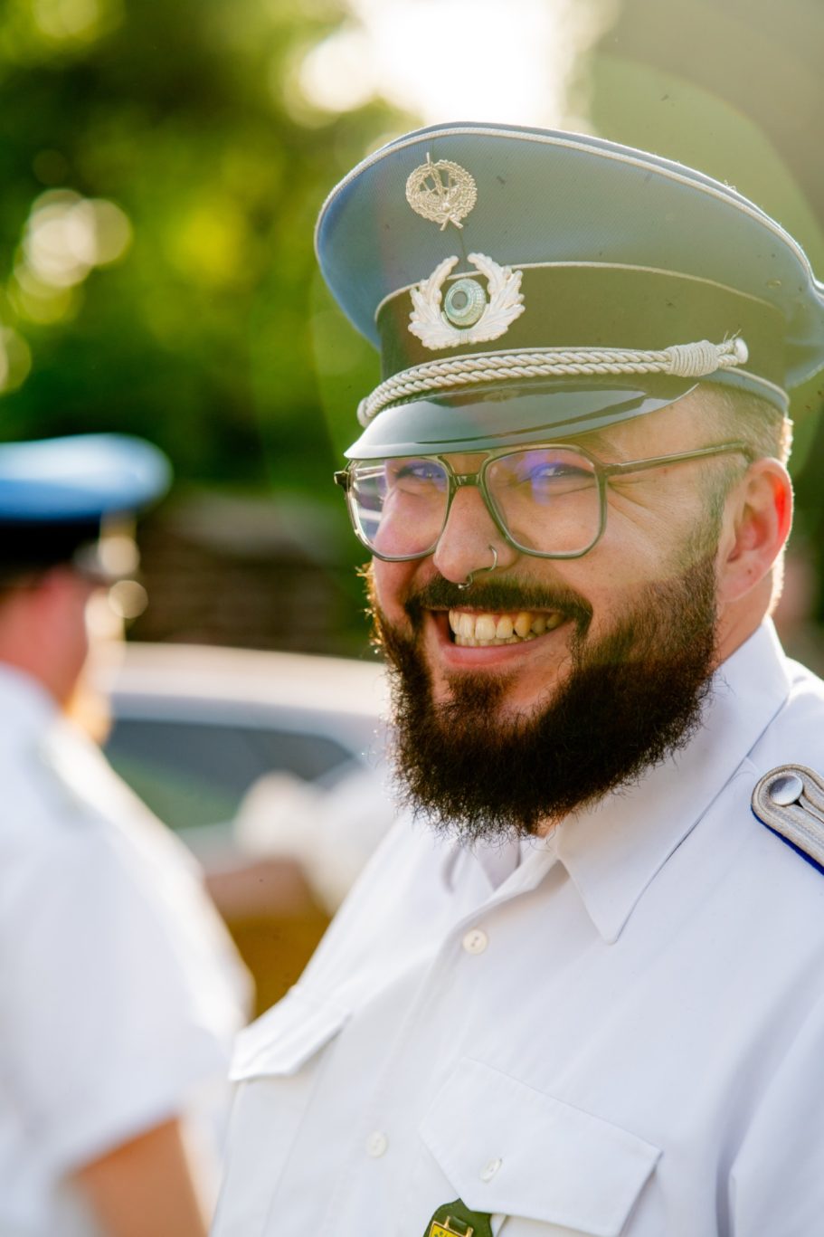Lächelnder Polizist in Uniform mit Brille und Hut, sonniger Hintergrund.