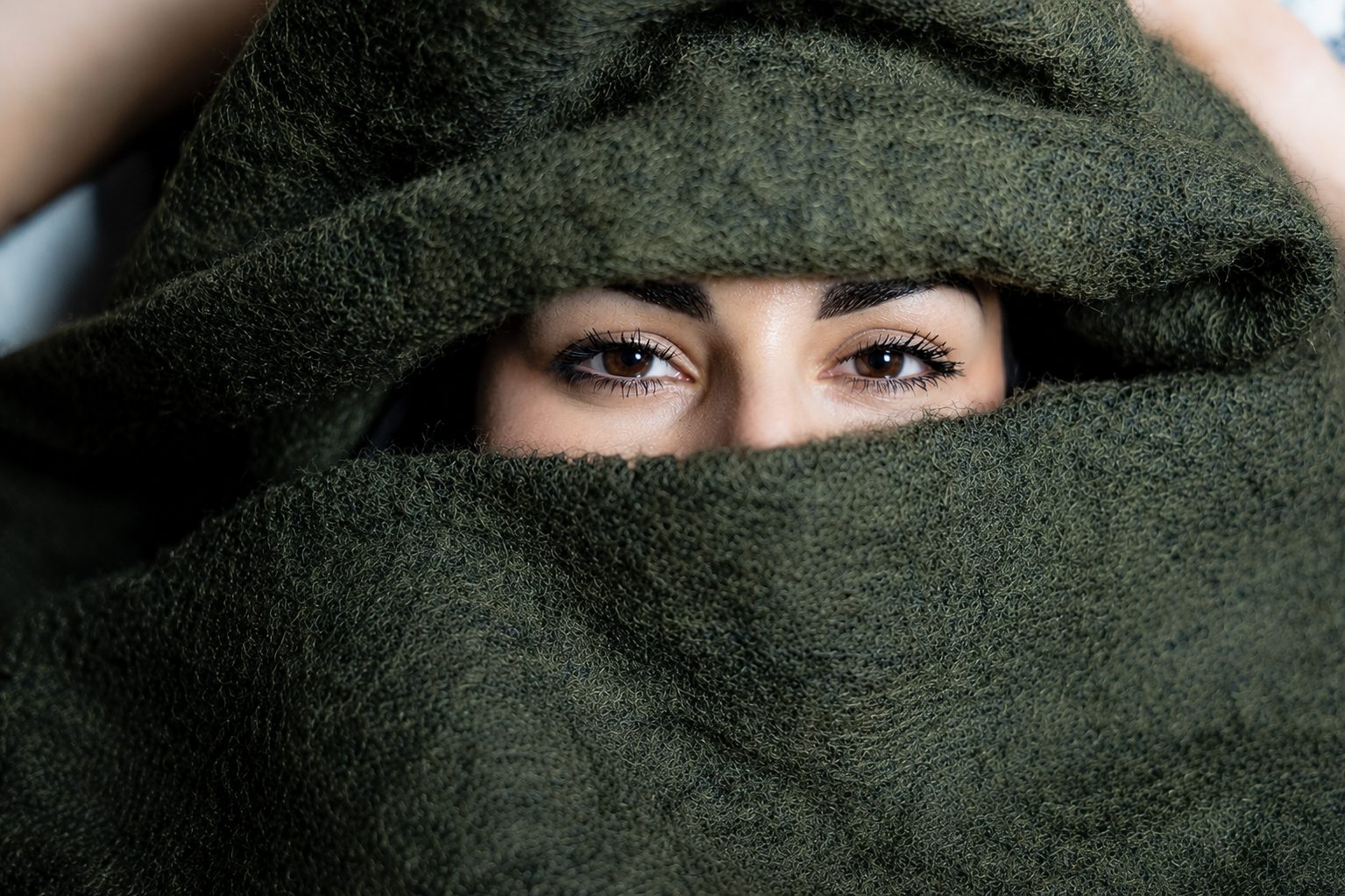 Junge Frau mit braunen Augen, eingehüllt in eine grüne Decke.