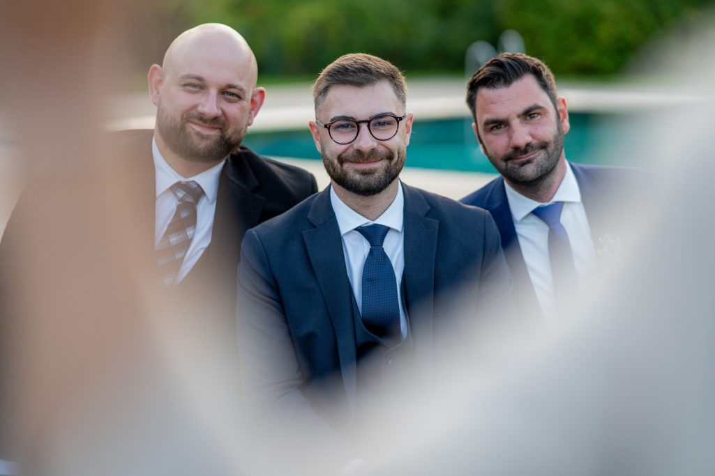 Drei Männer in Anzügen lächeln freundlich in die Kamera.