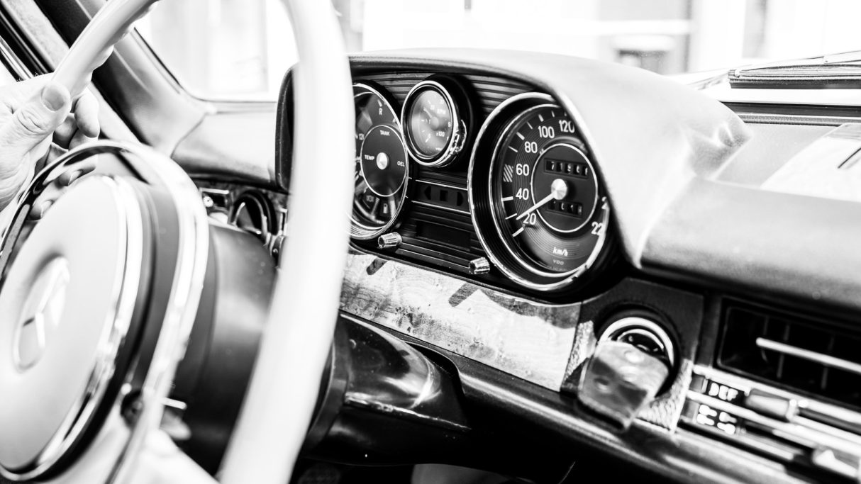 Innenansicht eines klassischen Autos mit analogen Instrumenten und einem weißen Lenkrad.