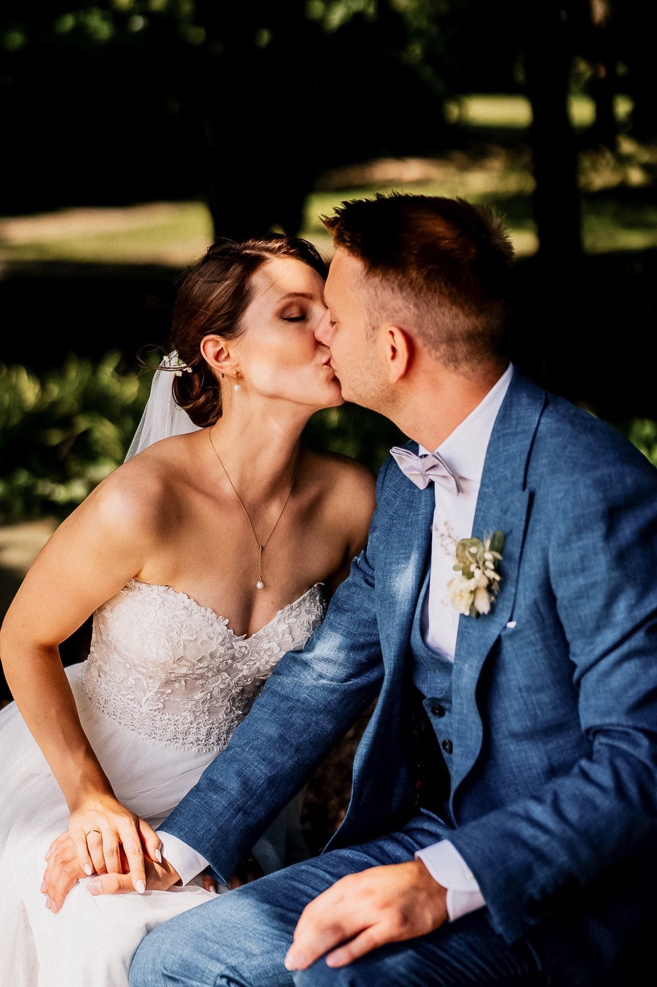 Ein Brautpaar küsst sich liebevoll im Freien, umgeben von grüner Natur.