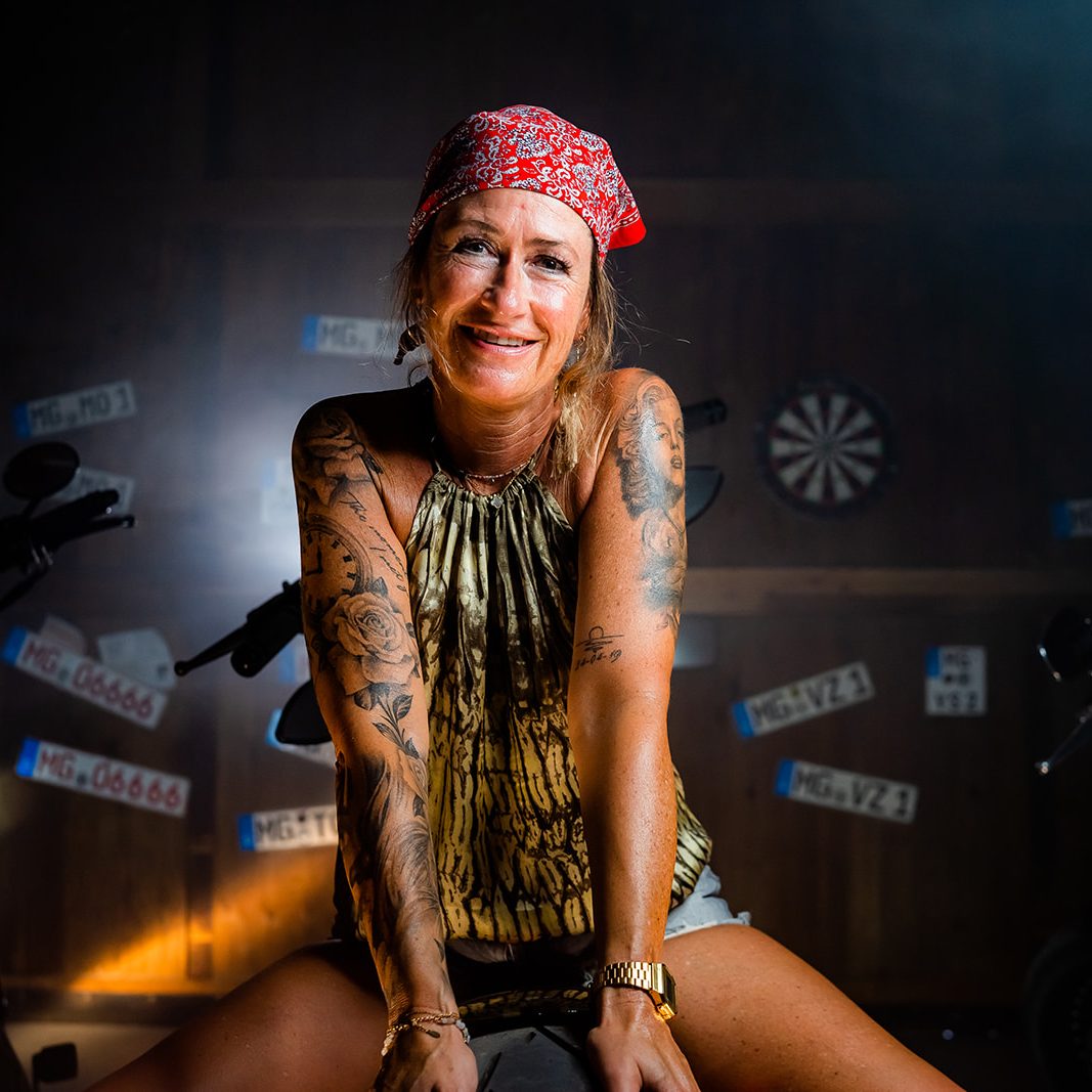 Frau mit Bandana und Tattoos lächelt in einer auffälligen, festlichen Umgebung.