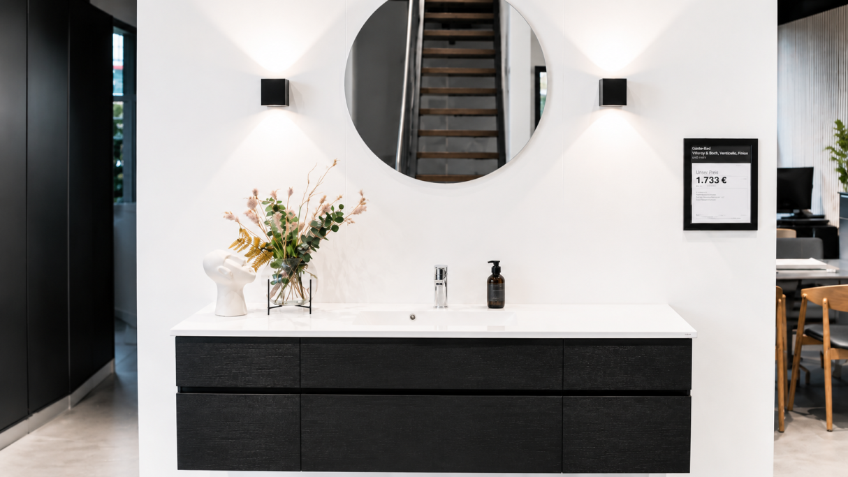 Moderne Badezimmeransicht mit schwarzem Waschtisch und rundem Spiegel, umgeben von Pflanzen.
