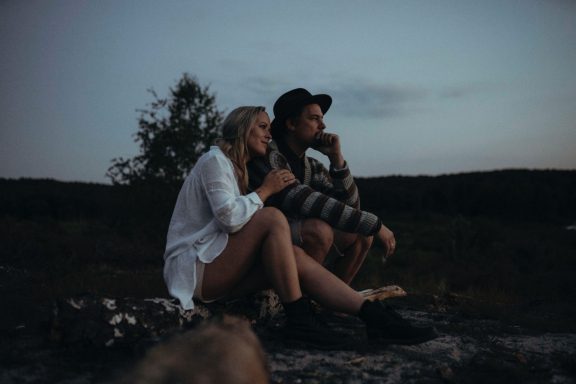 Ein Paar sitzt im Freien und schaut nachdenklich in die Ferne, umgeben von Natur.