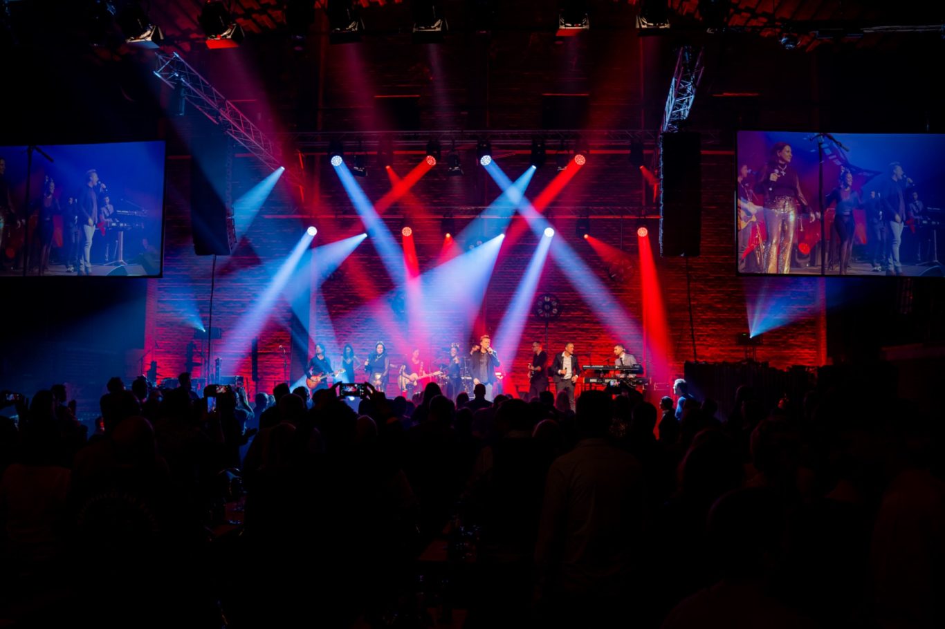 Bühne mit Band, farbige Lichter und begeistert feierndem Publikum.