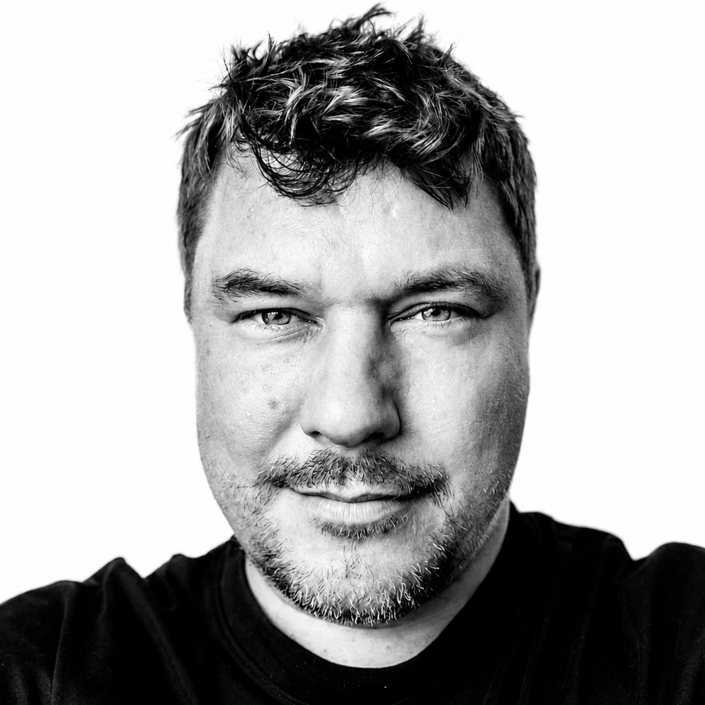 Mann mit kurzem, zerzaustem Haar und einem neutralen Gesichtsausdruck.