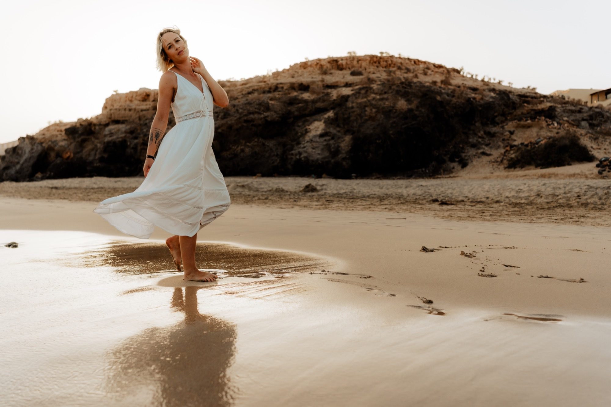 Frau in weißem Kleid, die fröhlich am Strand steht und ihr Kleid im Wind weht.