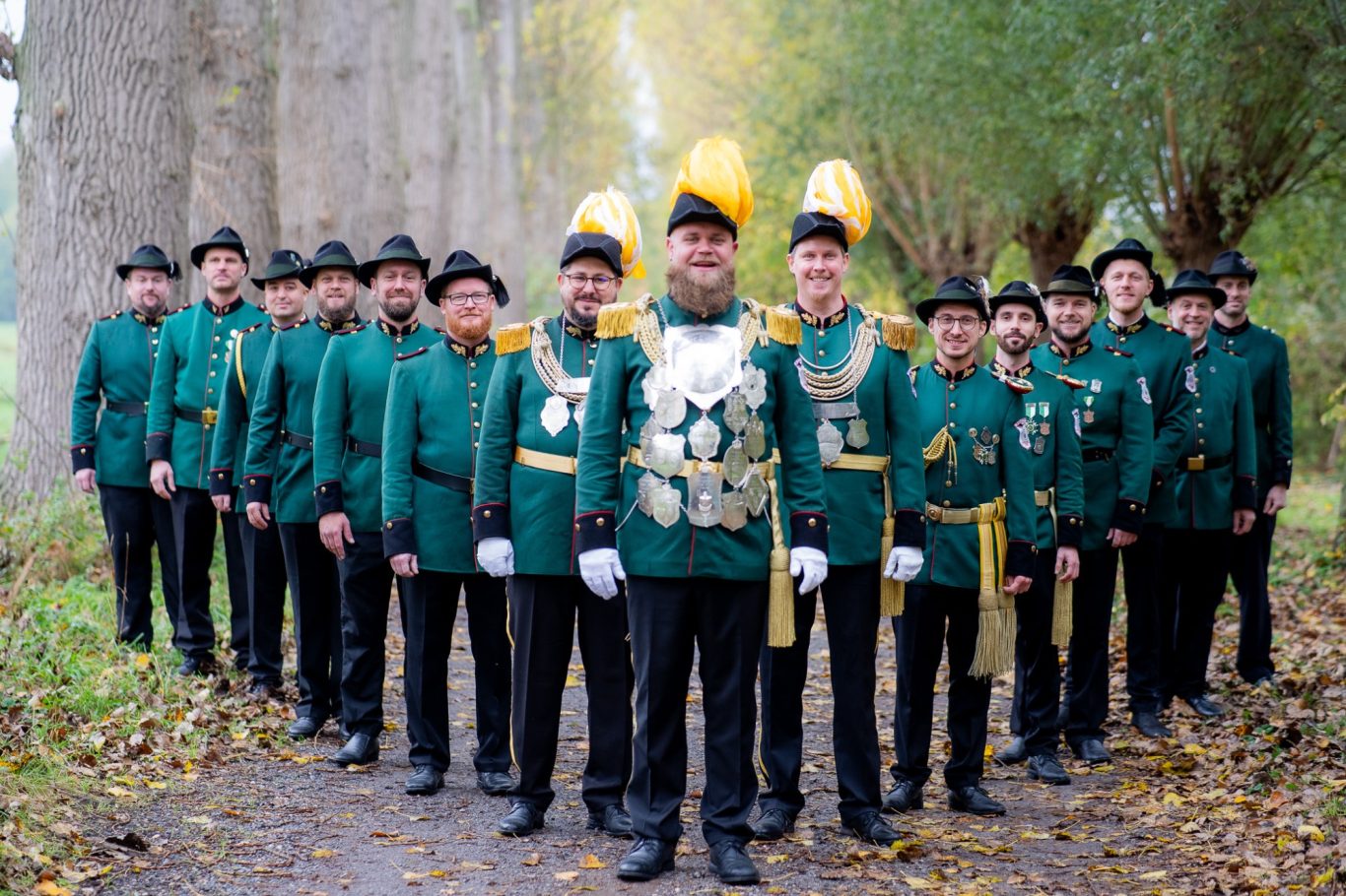 Gruppe von Männern in historischen Uniformen mit Hüten, auf einem Waldweg aufgestellt.