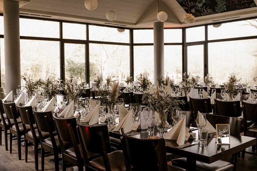 Elegant Restaurant mit gedeckten Tischen und Blumenarrangements an den Fenstern.