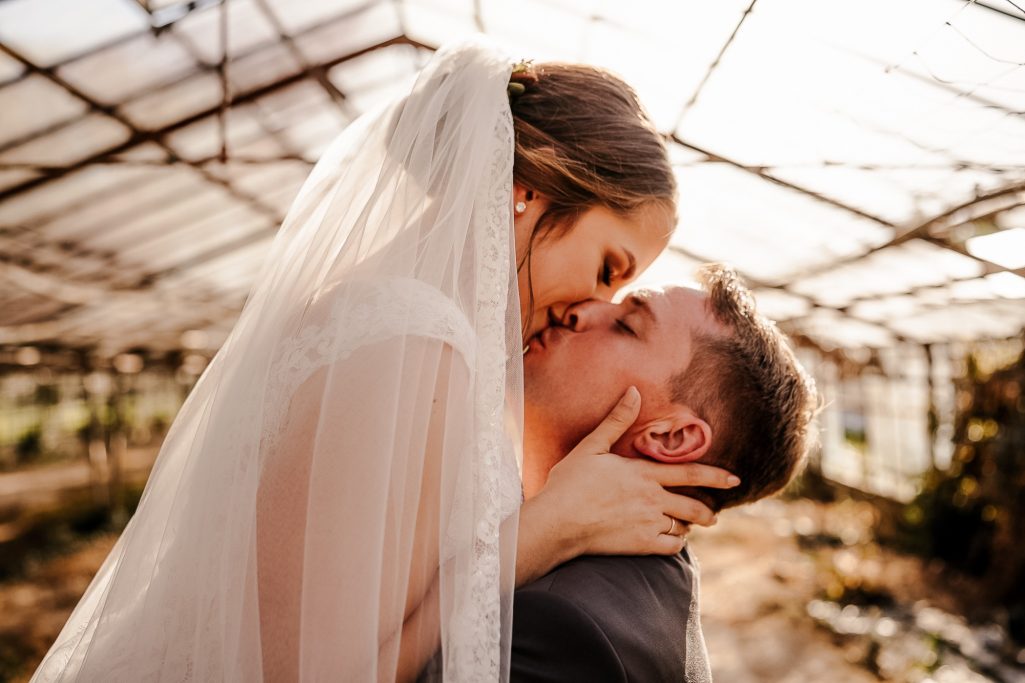 Braut und Bräutigam genießen einen innigen Moment unter einem Gewächshaus.