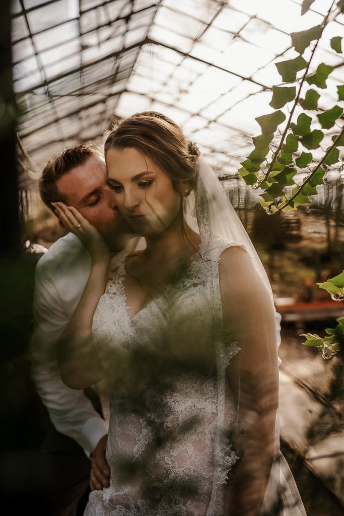 Brautpaar in einem Gewächshaus, umgeben von Pflanzen, romantischer Moment festgehalten.