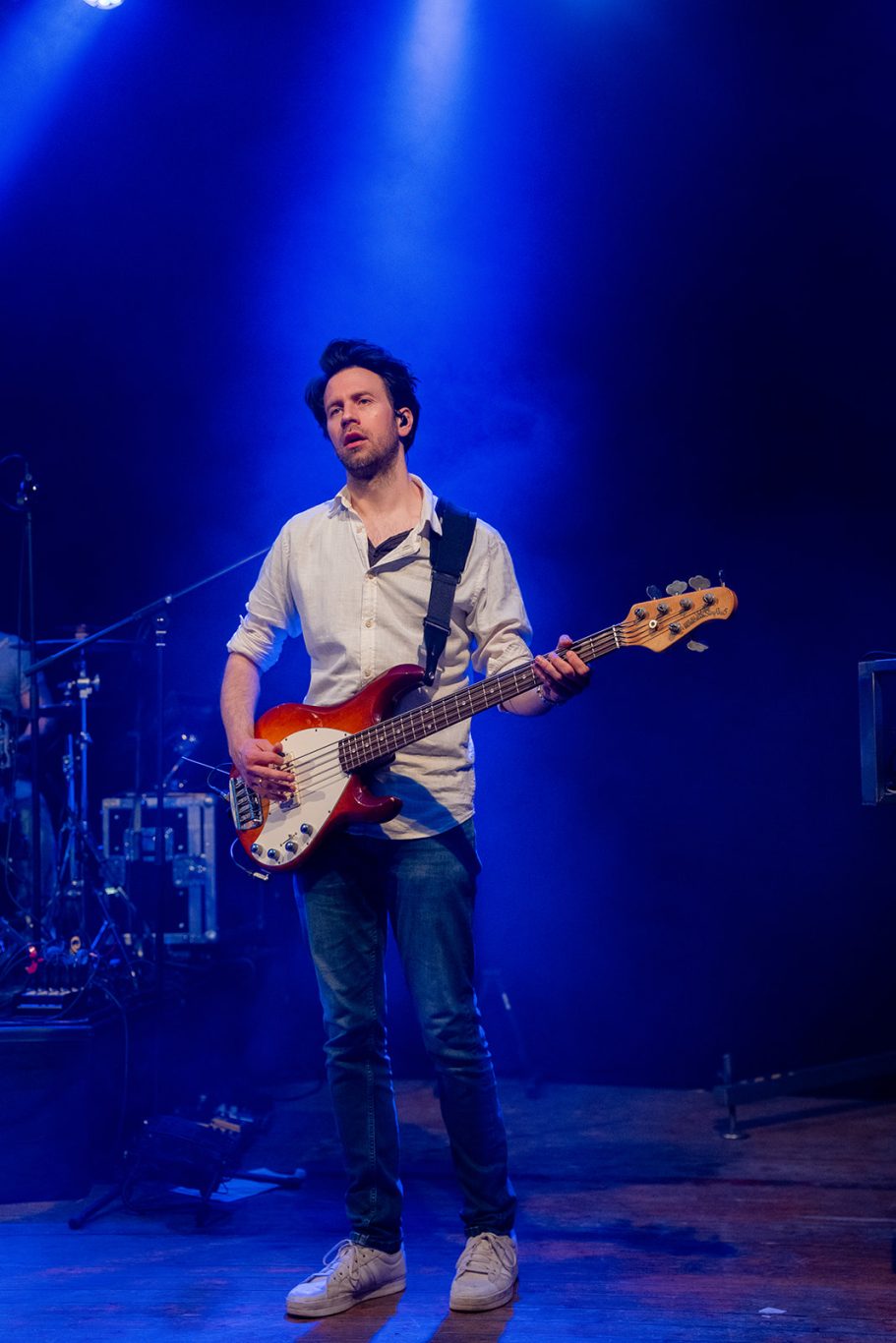 Mann mit E-Gitarre auf der Bühne, beleuchtet von blauen Scheinwerfern.