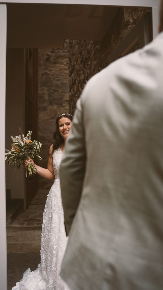 Braut mit Blumenstrauß in einem eleganten Hochzeitskleid steht vor einem Bräutigam.