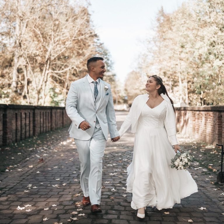 Brautpaar in eleganter Kleidung, Hand in Hand auf einem herbstlichen Weg.