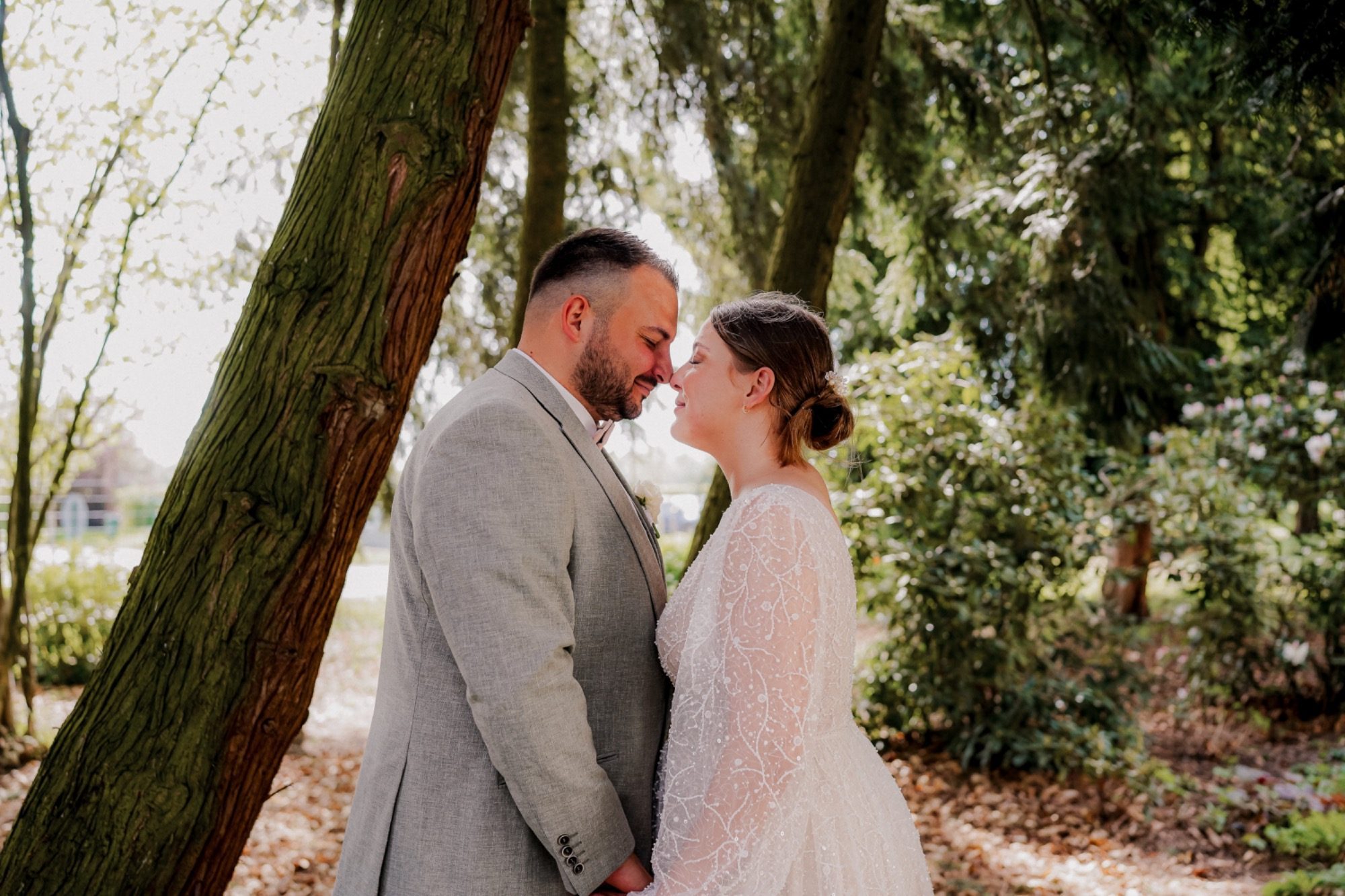 Ein Brautpaar steht sich unter Bäumen gegenüber und lächelt sich an.