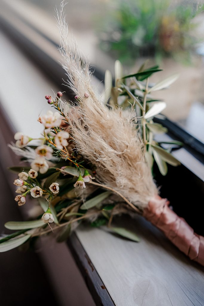 Ein Strauß aus getrockneten Blumen und Zierzweigen auf einem Fensterbrett.