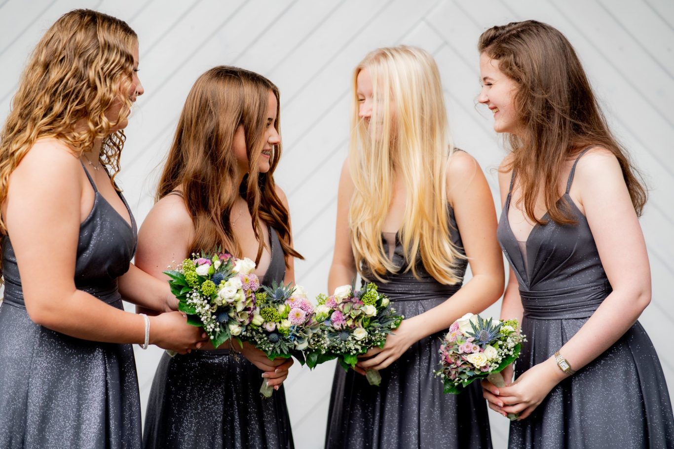 Vier Frauen in grauen Kleidern halten Blumensträuße und lächeln einander zu.