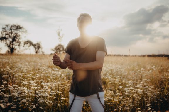 Mann im T-Shirt steht in einem blühenden Feld bei Sonnenuntergang.