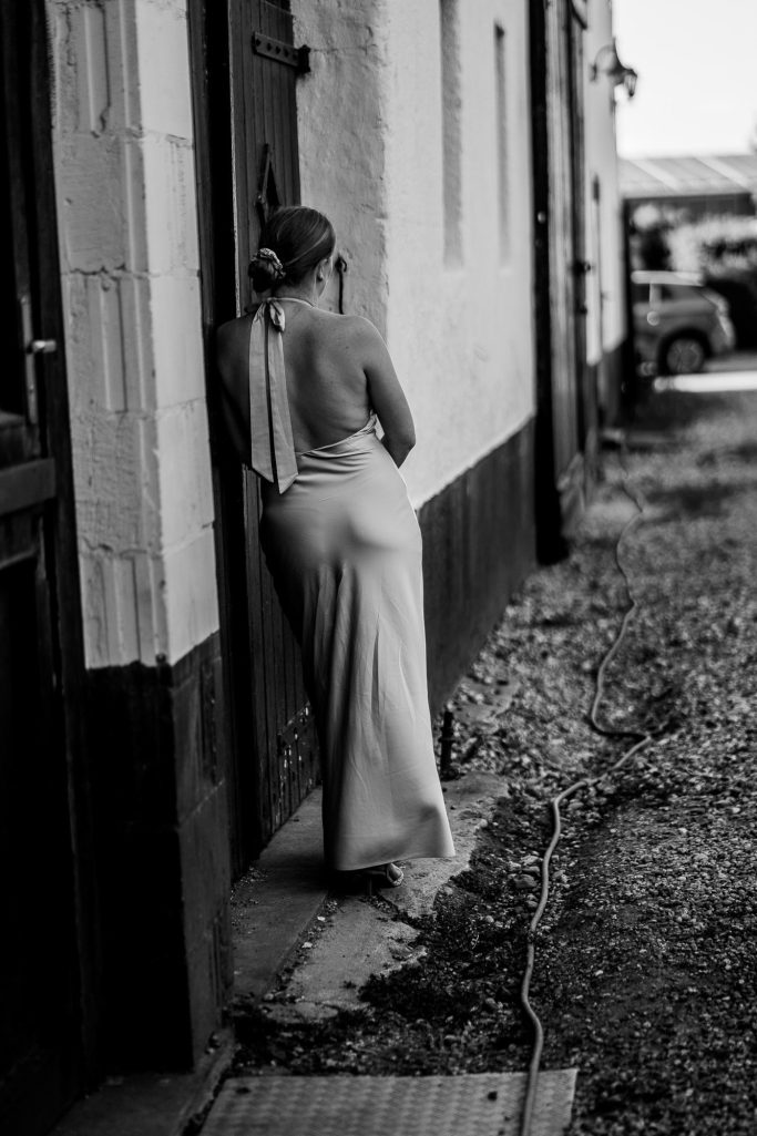 Frau in elegantem, schulterfreies Kleid lehnt an einer Wand.